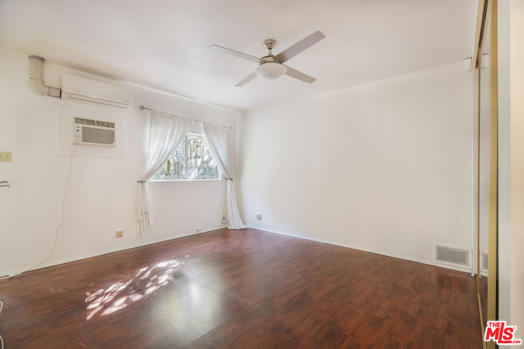 A light-filled secondary bedroom with original hardwood floors and arched window detail.