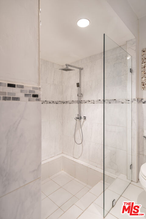 A renovated bath with marble shower, glass enclosure, and rain showerhead.