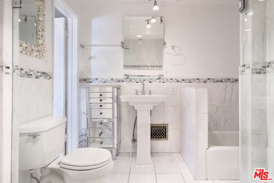 A marble-clad full bath with pedestal sink and tiled mosaic banding.