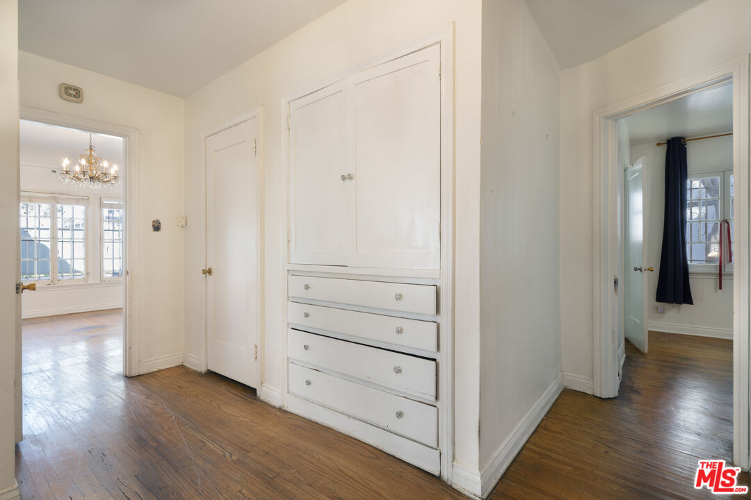 An interior hallway with built-in cabinetry, brass chandelier glimpsed beyond, and original hardwoods running the length.